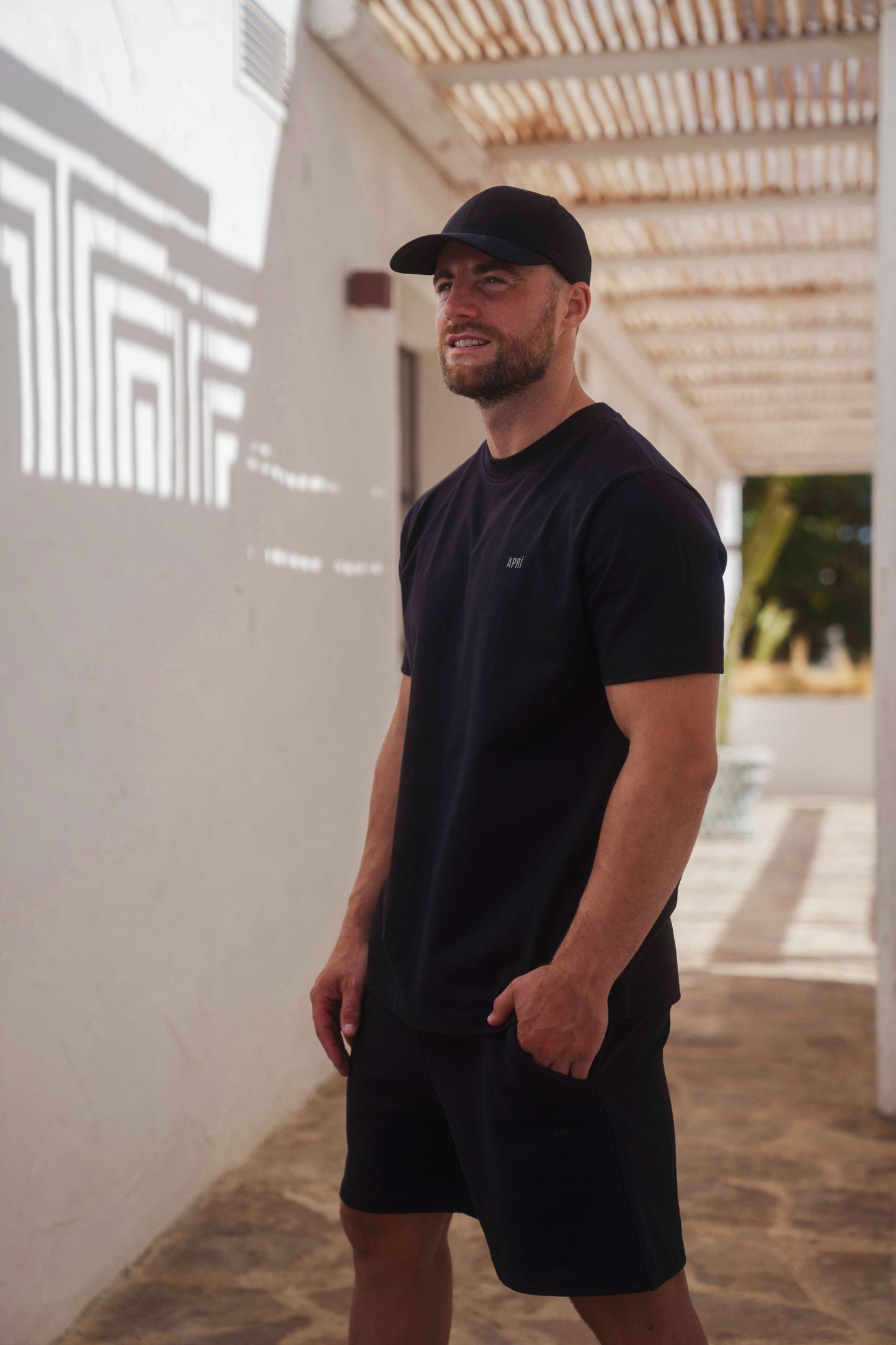 Man wearing a black t-shirt and shorts standing outdoors.