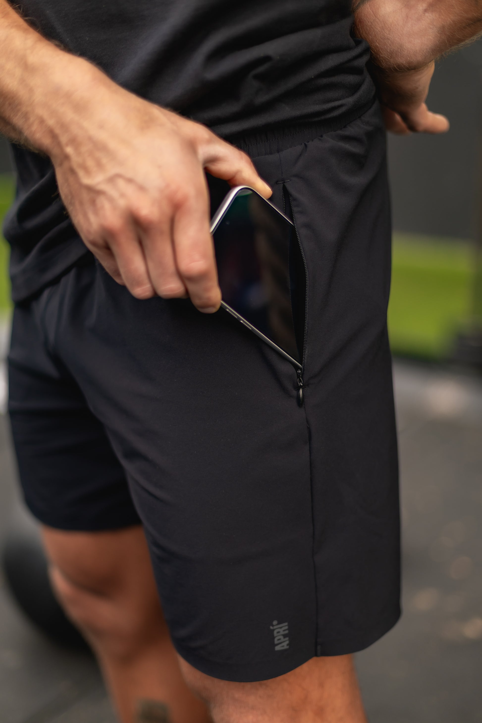 Person wearing black airy performance shorts with a pocket, holding a phone.