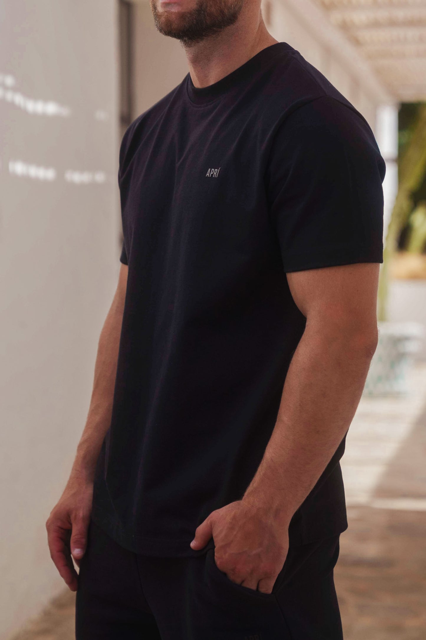 Man wearing a black t-shirt with a logo, standing against a neutral background.