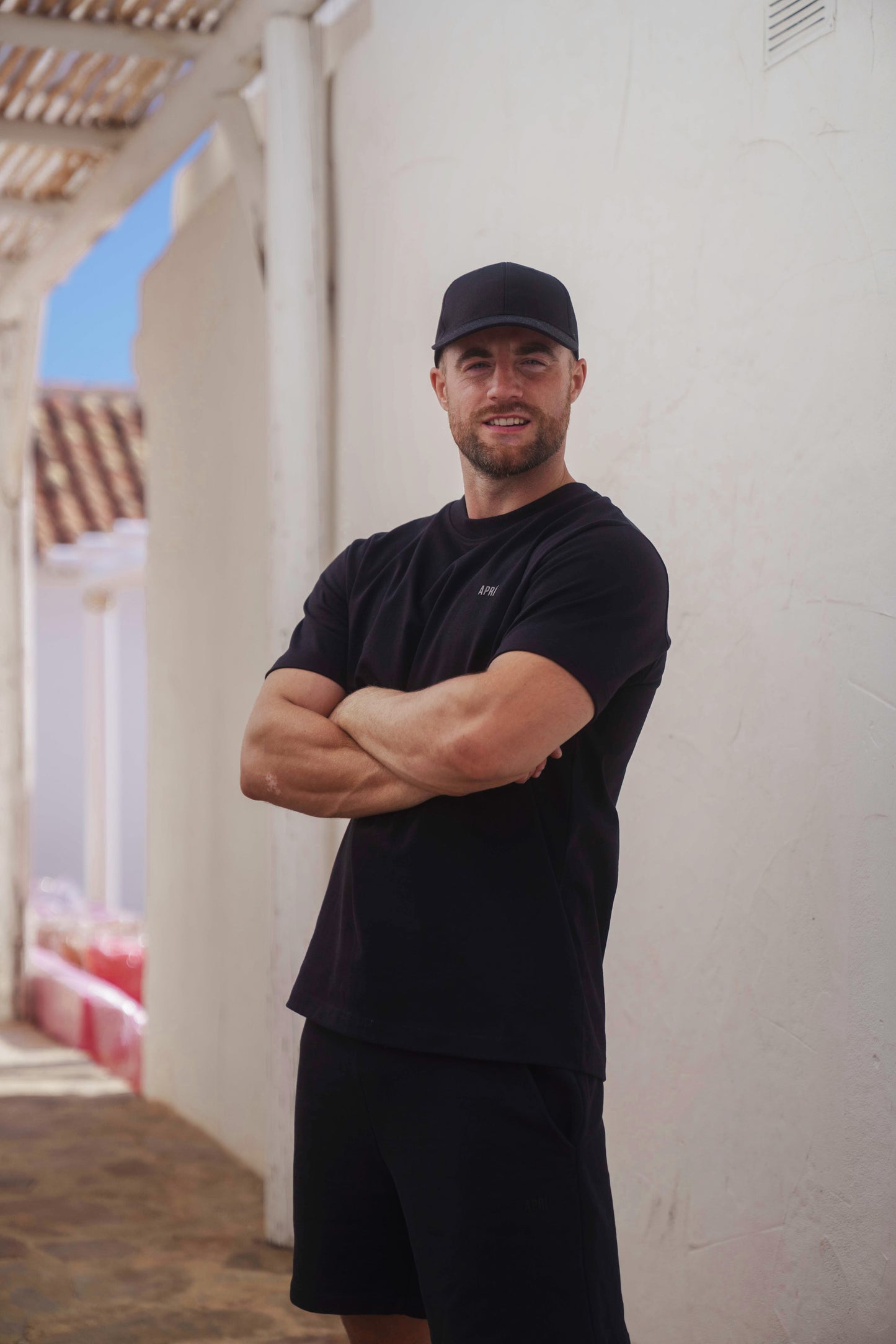 Man wearing a black cap and t-shirt standing against a white wall.