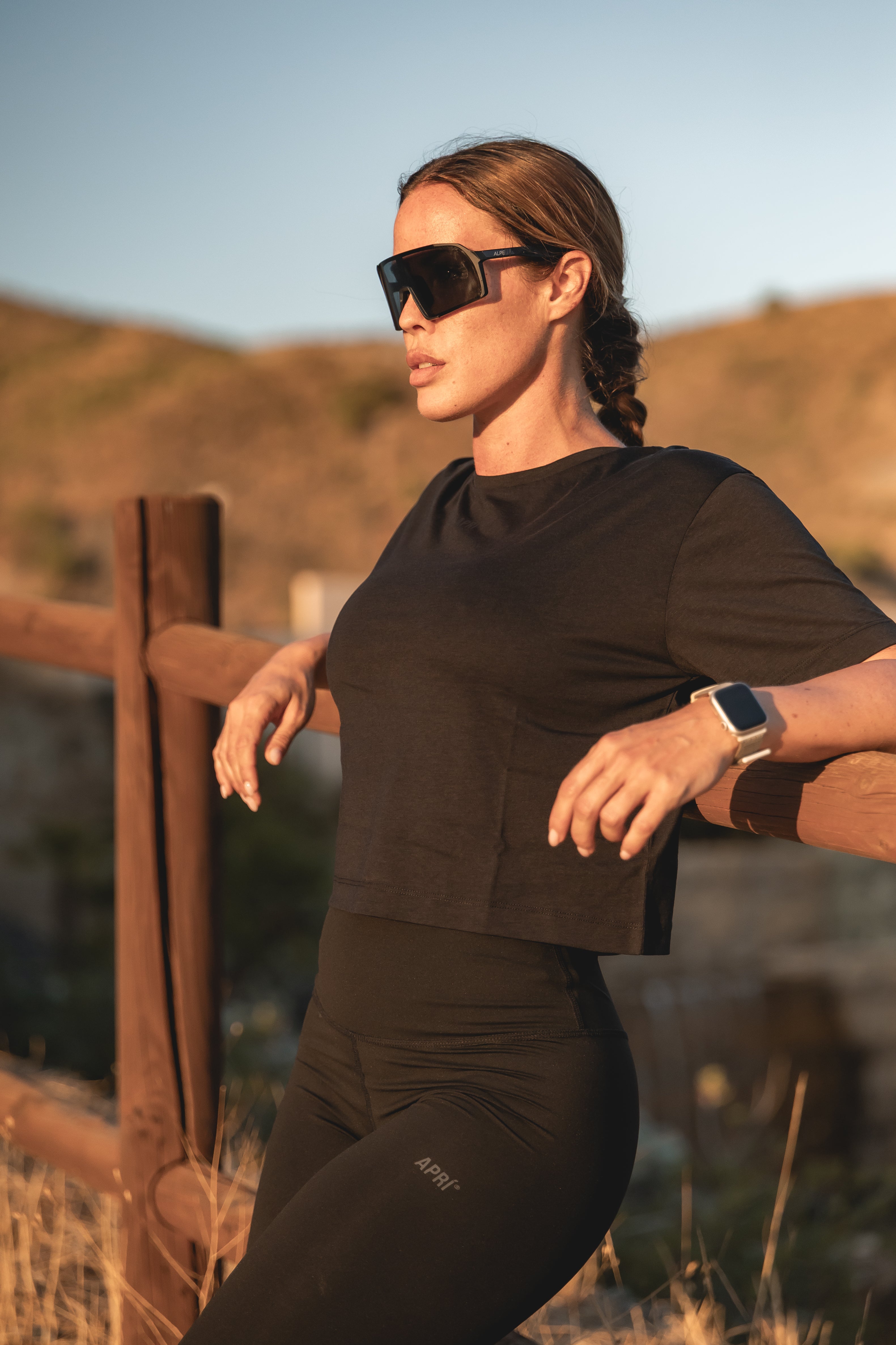 Person in black outfit with sunglasses and watch, standing outdoors.
